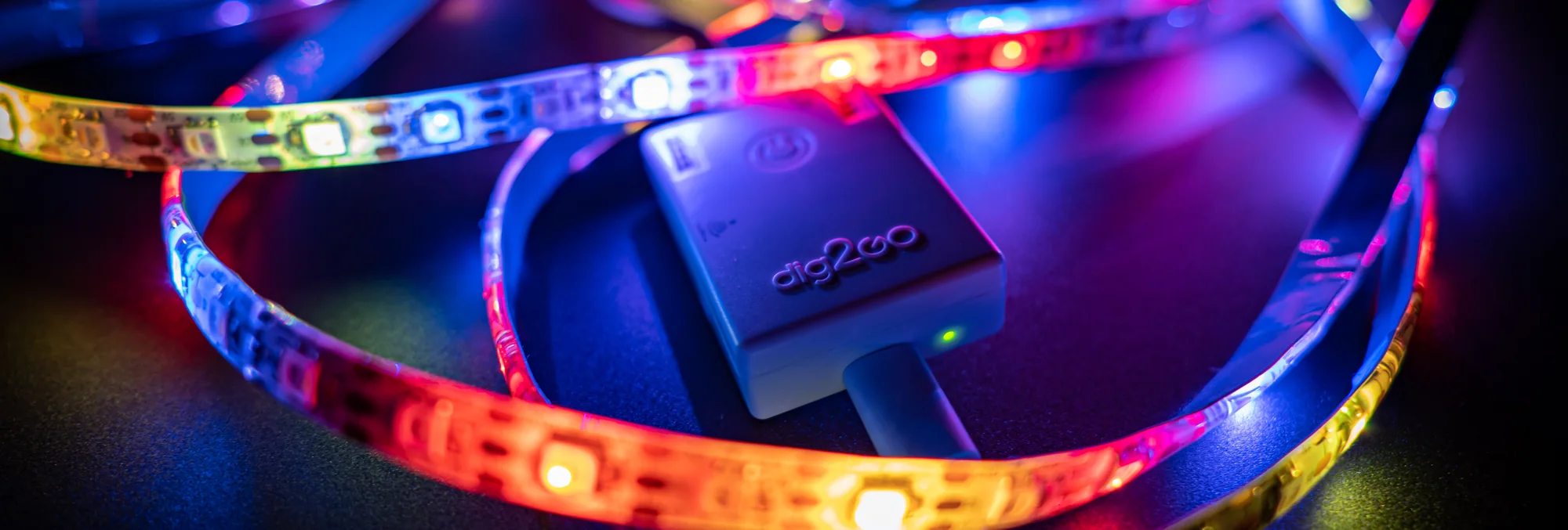 The white dig2go WLED controller surrounded by glowing addressable RGB LED strips on a dark surface
